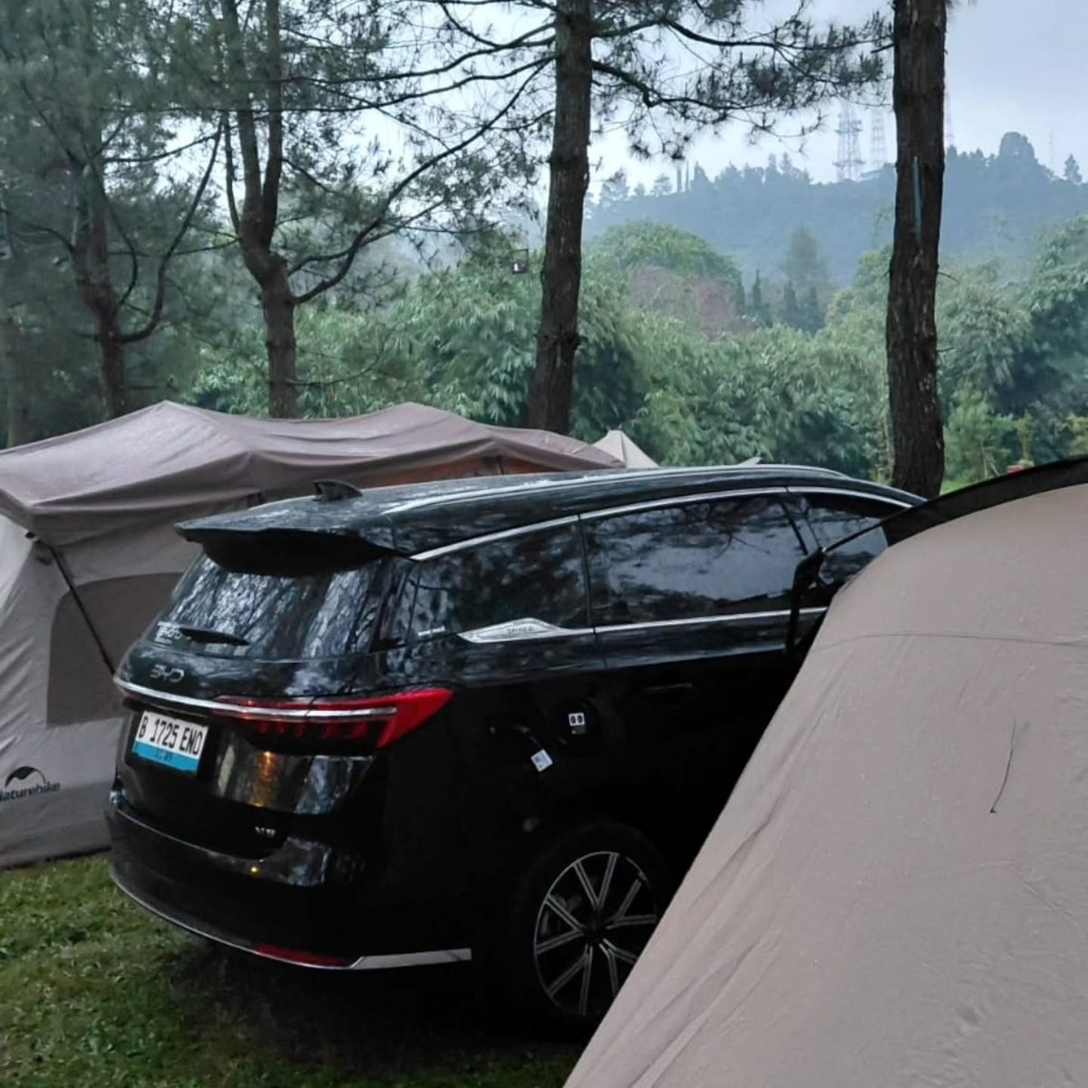 Mobil listrik di samping tenda di hutan berkabut