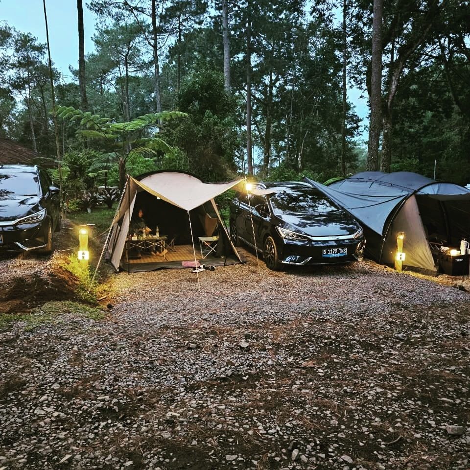 Tenda dan mobil listrik diterangi lampu camping saat senja