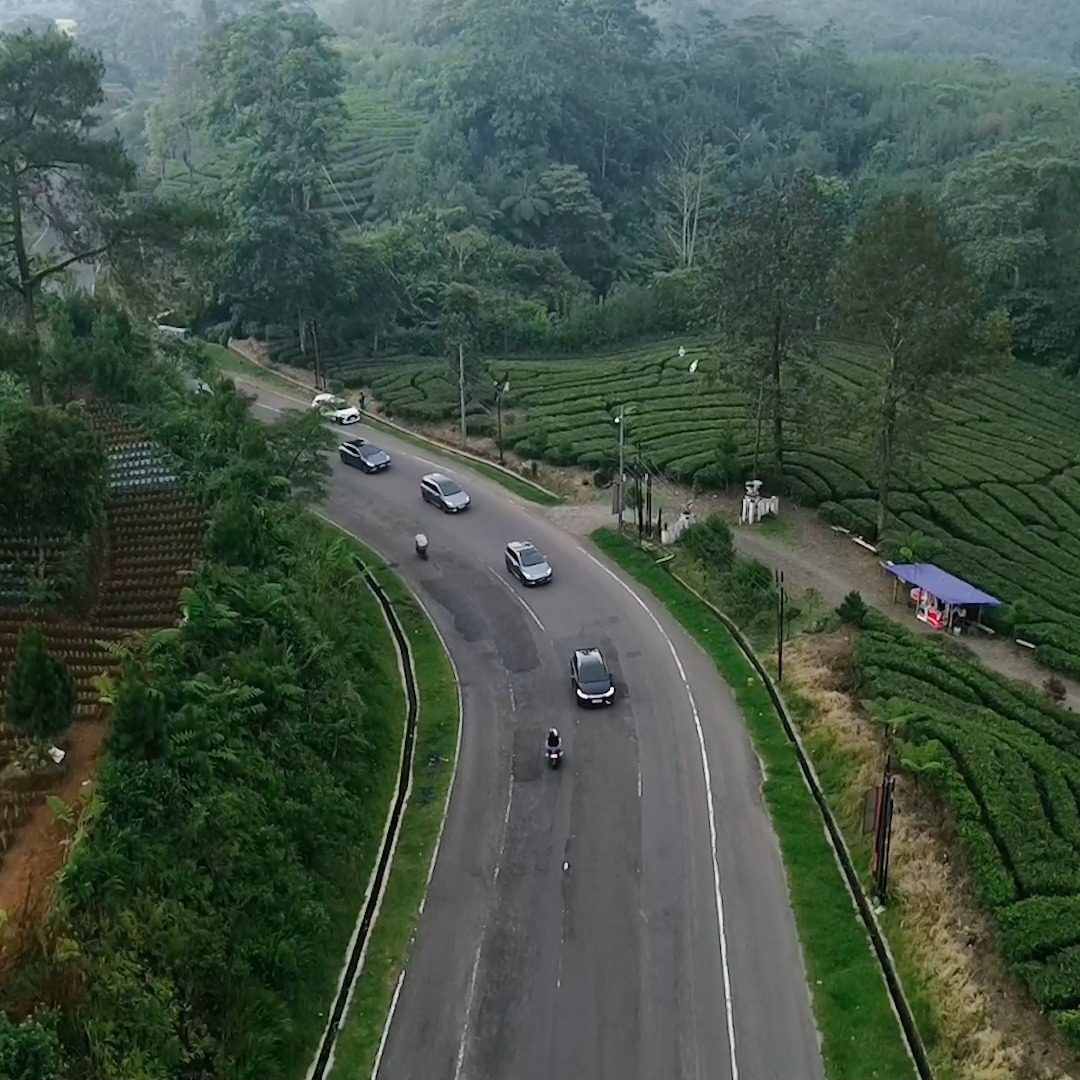 Konvoi mobil listrik di jalan berkelok, difoto dari udara